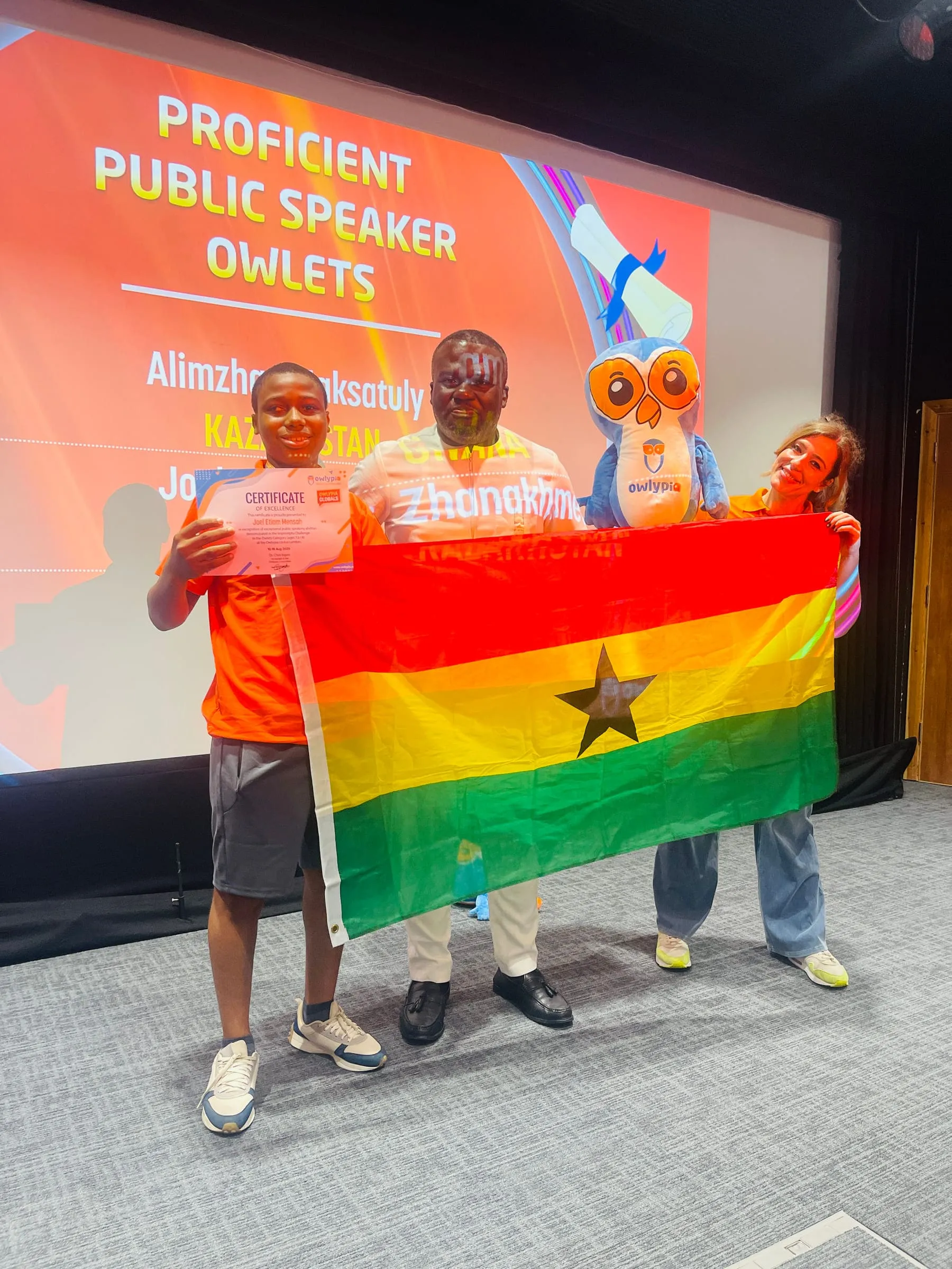 Joel Etiam Mensah holding his Owlypia Certificate of Excellence and the Ghanaian flag at Owlypia Global London